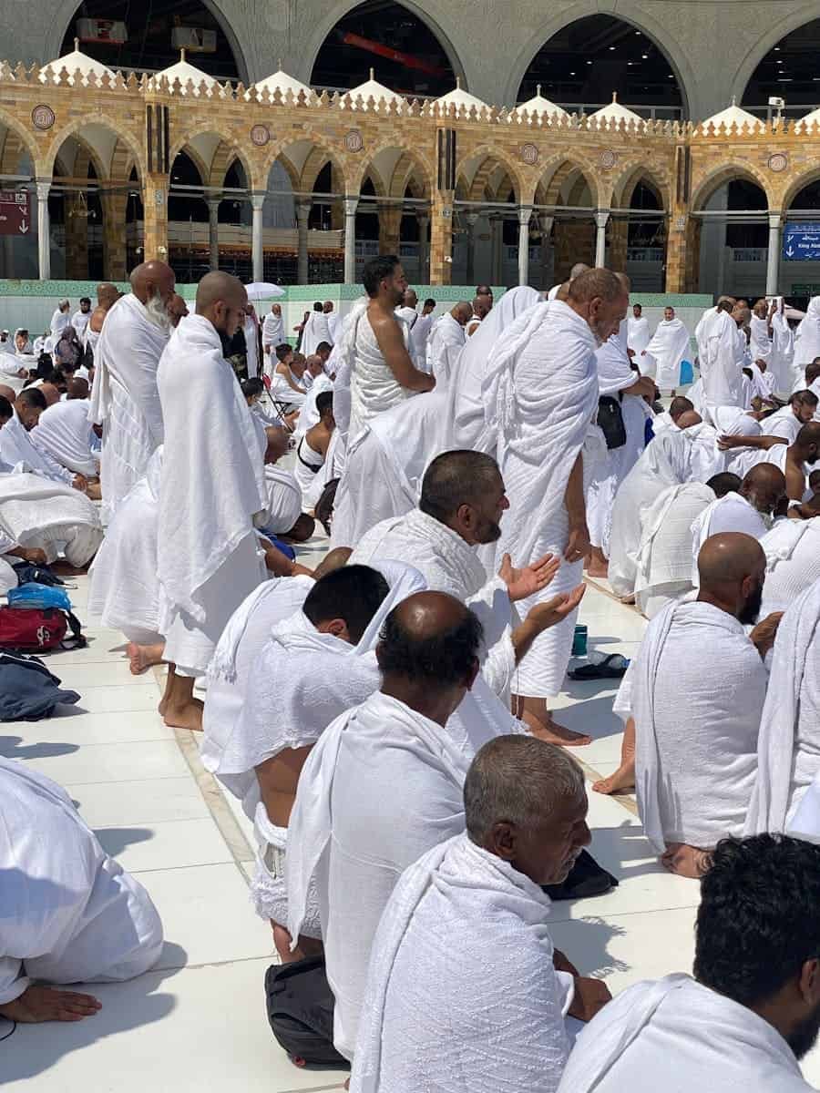 A gathering of pilgrims in white ihram garments praying at Masjid al-Haram, Mecca.