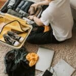 Man organizing clothes and essentials into a yellow suitcase for travel in a cozy living room.