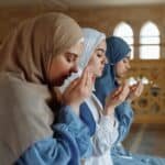 Three women in hijab engage in prayer inside a mosque, reflecting spirituality and faith.