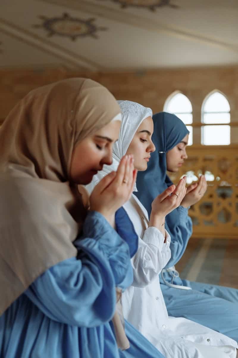 Three women in hijab engage in prayer inside a mosque, reflecting spirituality and faith.